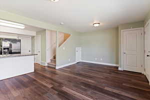 Unfurnished living room with baseboards, stairs, dark wood-type flooring, and a sink