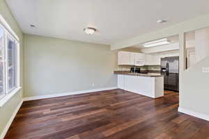 Kitchen featuring stainless steel refrigerator with ice dispenser, white microwave, dark countertops, a peninsula, and black range with electric cooktop