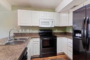 Kitchen featuring black appliances, a sink, white cabinets, and wood finished floors