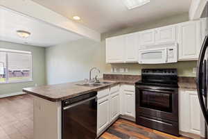 Kitchen with white microwave, dishwasher, electric range, a sink, and a peninsula
