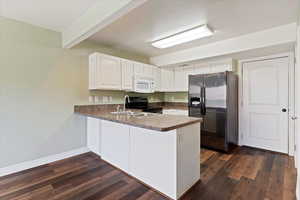 Kitchen with stainless steel refrigerator with ice dispenser, white microwave, a sink, a peninsula, and black range with electric stovetop