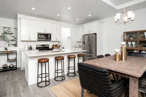 Kitchen with appliances with stainless steel finishes, a sink, a breakfast bar, light wood finished floors, and a chandelier