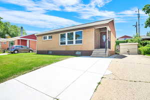 View of front facade with brick, front lawn area, widened driveway with view to the backyard.
