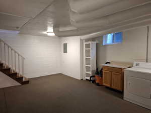 Basement with washer / clothes dryer, electric panel, dark colored carpet, stairs, and concrete block wall