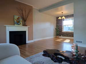Living room featuring a chandelier, wood finished floors, ornamental molding, and a fireplace with flush hearth