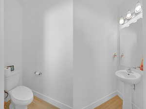 Half bathroom with wood finished floors, baseboards, and toilet