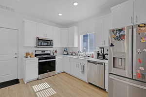 Kitchen with appliances with stainless steel finishes, a sink, light wood-style floors, light countertops, and white cabinetry