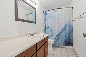 Full bathroom featuring toilet, vanity, tile patterned flooring, and curtained shower