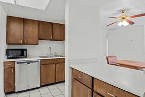 Kitchen featuring dishwasher, black microwave, a sink, light countertops, and light tile patterned floors