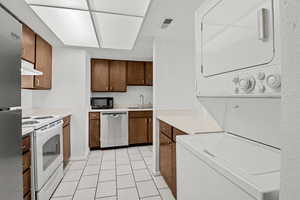 Kitchen with appliances with stainless steel finishes, estacked washer and dryer, a sink, under cabinet range hood, and light countertops