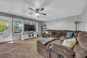 Living area with light colored carpet, a ceiling fan, baseboards, and a textured ceiling