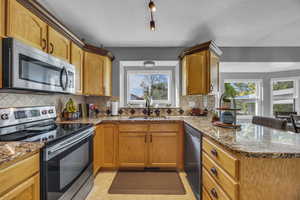 Kitchen featuring appliances with stainless steel finishes, a sink, a peninsula, stone countertops, and tasteful backsplash