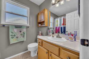 Full bathroom featuring tile patterned flooring, vanity, toilet, baseboards, and a shower with shower curtain