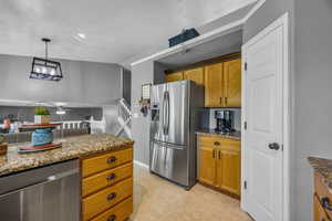 Kitchen featuring stainless steel appliances, dark stone counters, brown cabinets, a ceiling fan, and pendant lighting