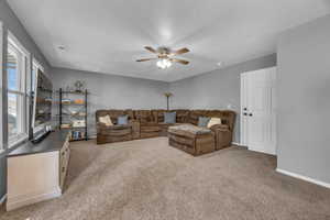 Carpeted living room featuring ceiling fan, baseboards, and a textured ceiling