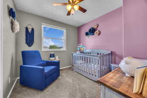 Bedroom with carpet floors, a nursery area, baseboards, ceiling fan, and a textured ceiling