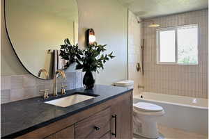 Full bathroom featuring a textured ceiling, vanity, toilet, washtub / shower combination, and backsplash
