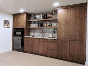 Indoor wet bar with light wood finished floors, baseboards, recessed lighting, and beverage cooler