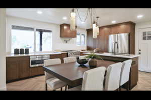Kitchen with stainless steel appliances, light countertops, hanging light fixtures, a kitchen island with sink, and recessed lighting