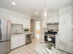 Kitchen featuring appliances with stainless steel finishes, a sink, under cabinet range hood, light tile patterned flooring, and light countertops