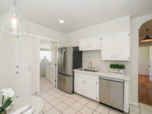 Kitchen with stainless steel appliances, a sink, white cabinets, light countertops, and crown molding