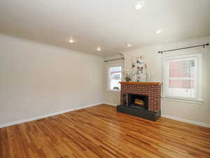 Unfurnished living room featuring light wood-style flooring, a brick fireplace, baseboards, and recessed lighting