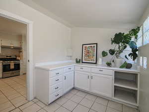 Kitchen with gas stove, light tile patterned floors, under cabinet range hood, white cabinets, and vaulted ceiling