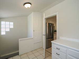 Kitchen featuring freestanding refrigerator, light tile patterned flooring, white cabinets, and light countertops