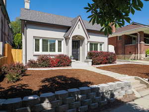 View of front facade with a chimney, roof with shingles, and stucco siding