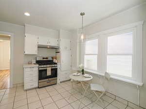 Kitchen featuring stainless steel range with gas stovetop, under cabinet range hood, light countertops, white cabinets, and crown molding