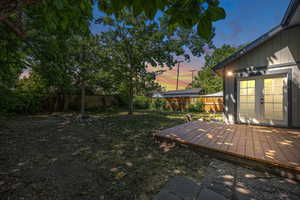 Yard at dusk with french doors, a fenced backyard, and a deck