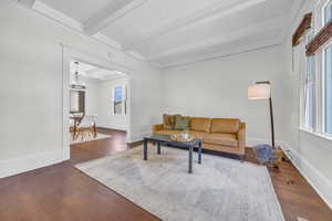 Living room featuring beam ceiling, dark wood-style floors, baseboards, a chandelier, and ornamental molding