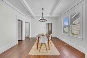 Dining area featuring a chandelier, dark wood-style floors, beamed ceiling, baseboards, and coffered ceiling
