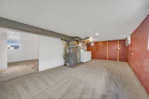 Below grade area featuring carpet floors, brick wall, heating unit, baseboards, and washing machine and clothes dryer