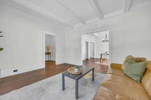Living area featuring beam ceiling, wood finished floors, a chandelier, crown molding, and baseboards