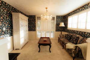 Living area featuring wallpapered walls, a chandelier, healthy amount of natural light, a wainscoted wall, and baseboards