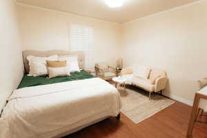 Bedroom with wood finished floors, crown molding, and baseboards