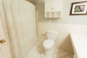 Full bathroom featuring toilet, a wainscoted wall, tile patterned flooring, curtained shower, and tile walls