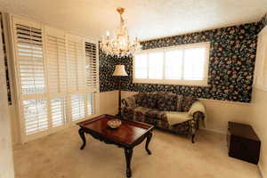 Living room with wallpapered walls, a chandelier, carpet, a textured ceiling, and wainscoting
