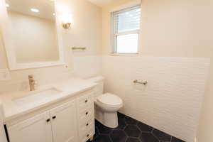 Bathroom featuring tile walls, toilet, vanity, tile patterned floors, and a wainscoted wall
