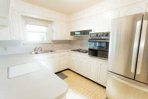 Kitchen featuring black appliances, a sink, range hood, light flooring, and light countertops