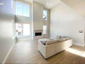 Living room featuring high vaulted ceiling, light wood-style flooring, baseboards, and a large fireplace
