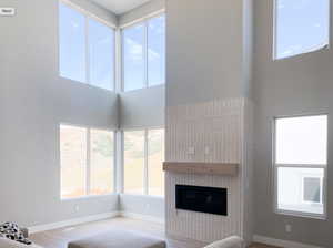 Unfurnished living room featuring a towering ceiling, baseboards, a glass covered fireplace, and wood finished floors