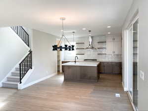 Kitchen with open shelves, range hood, light wood-style flooring, light countertops, and a sink