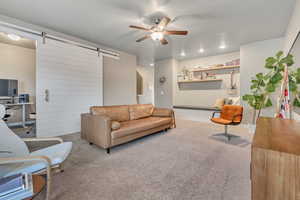 Living room with a barn door, ceiling fan, and carpet floors