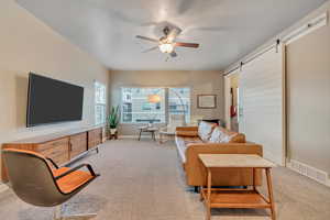 Living room with light carpet, a barn door, a ceiling fan, and baseboards