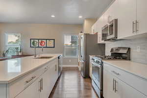 Kitchen with appliances with stainless steel finishes, a sink, light countertops, dark wood finished floors, and decorative backsplash