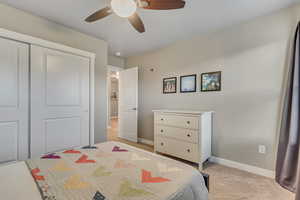 Bedroom with light carpet, baseboards, a closet, and a ceiling fan