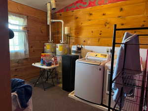 Washroom featuring washer and clothes dryer, water heater, wood walls, and carpet flooring