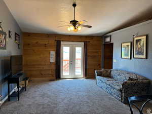 Carpeted living room with french doors, a textured ceiling, wooden walls, and ceiling fan